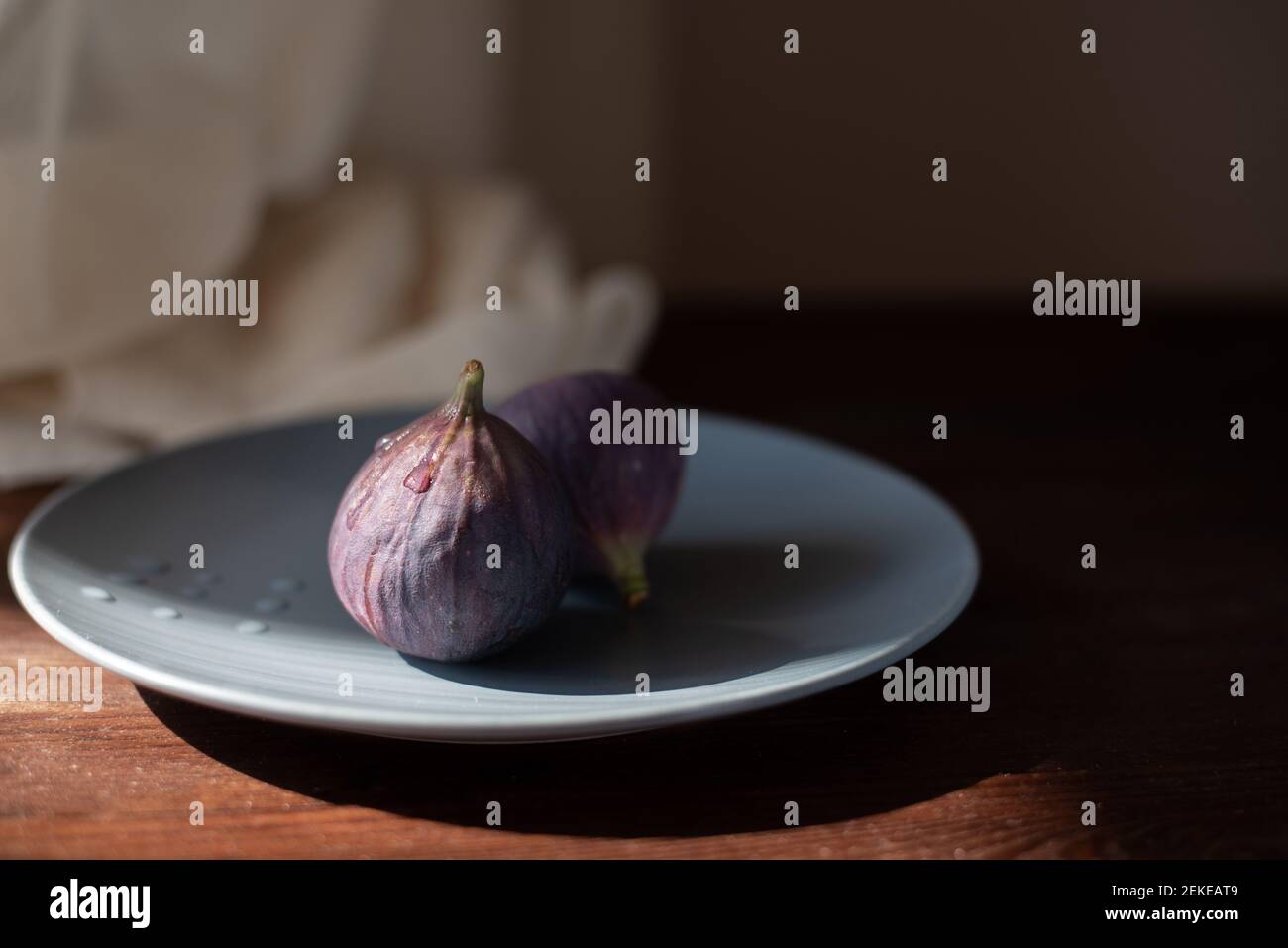 deux figues dans une plaque en céramique sur la table en bois au soleil. Banque D'Images