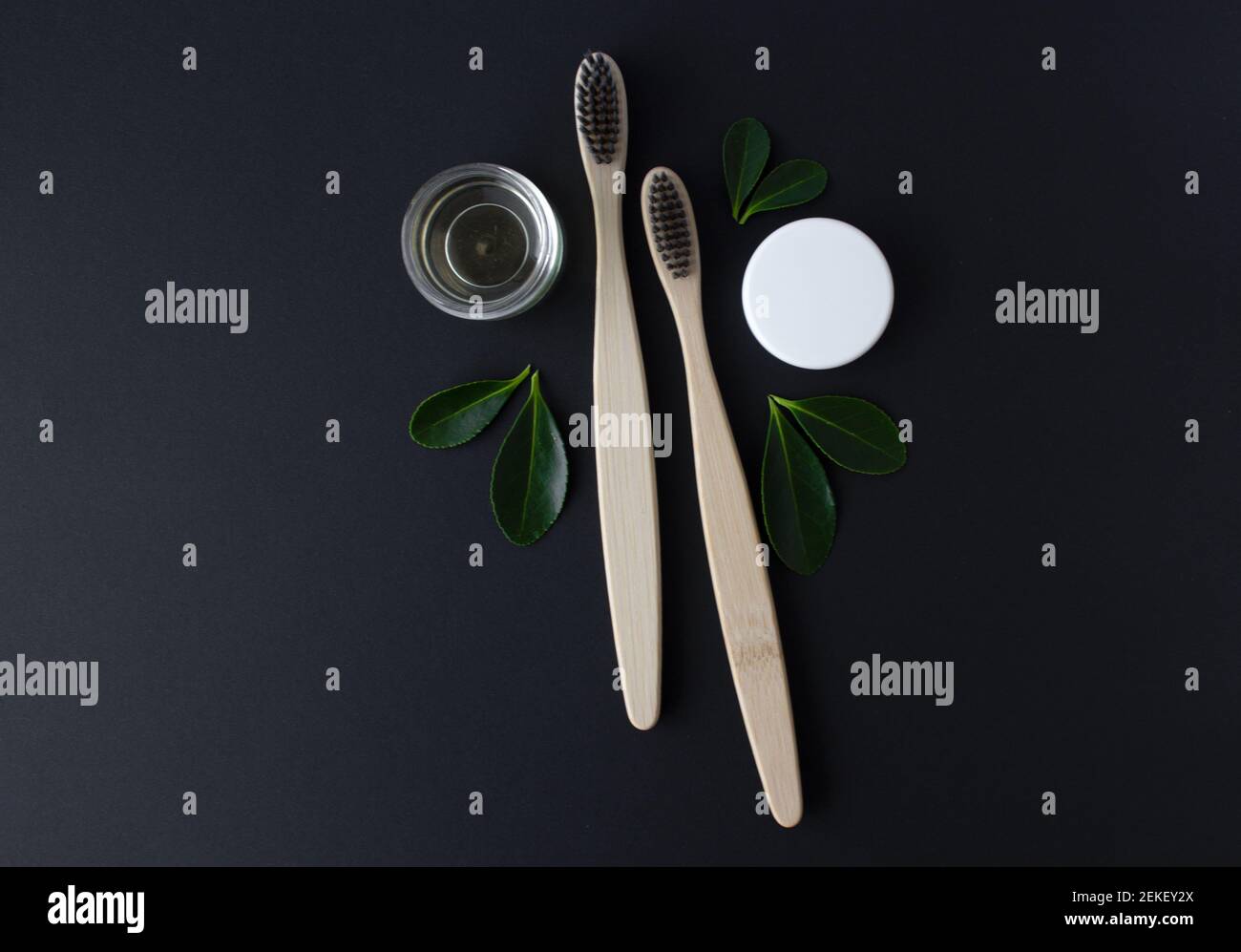 deux brosses à dents écologiques en bambou en bois, dentifrice et feuilles vertes sur fond noir. Banque D'Images