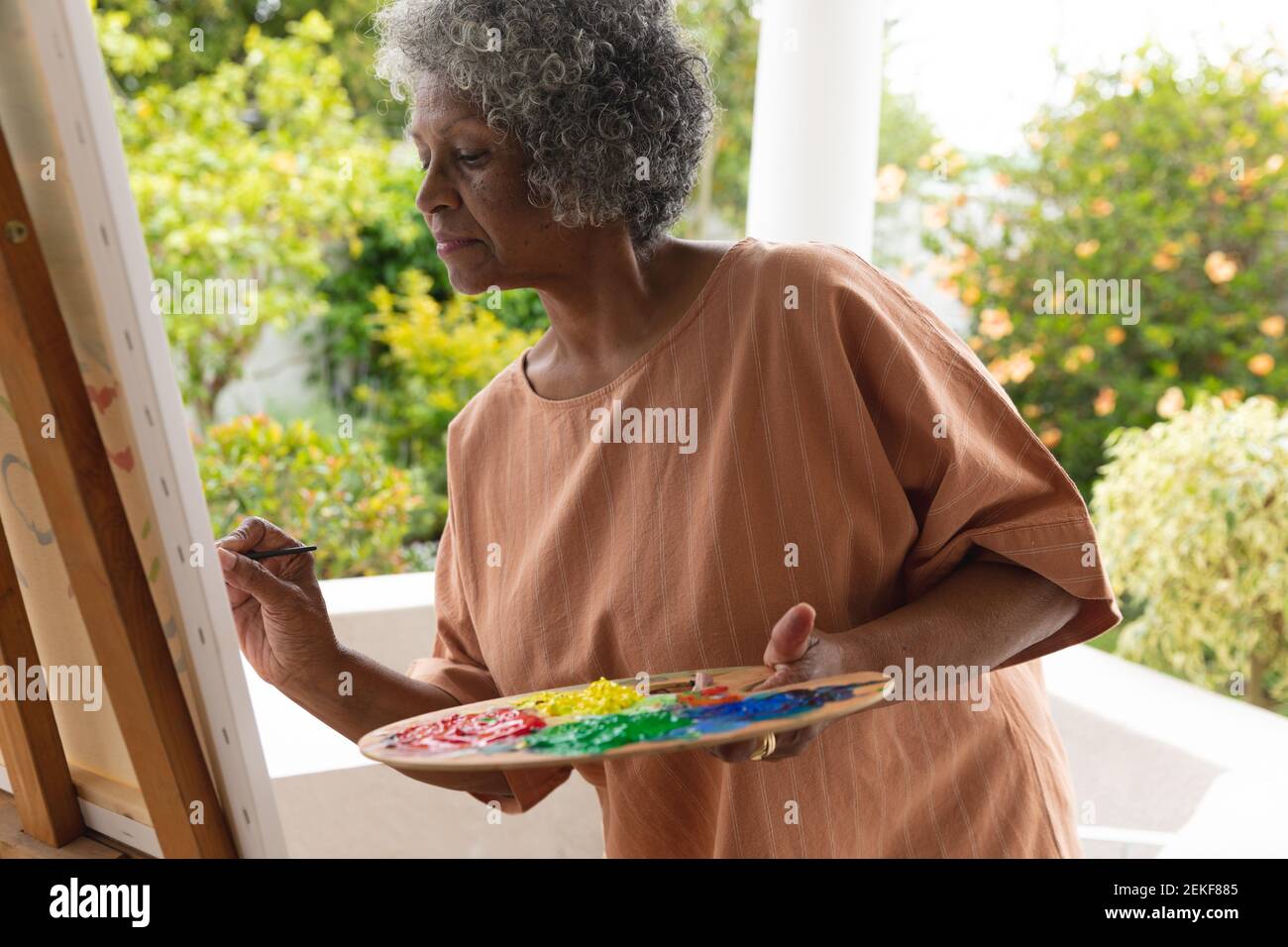 Femme afro-américaine réfléchie peint sur toile pendant qu'elle se tient debout sur le porche de la maison Banque D'Images