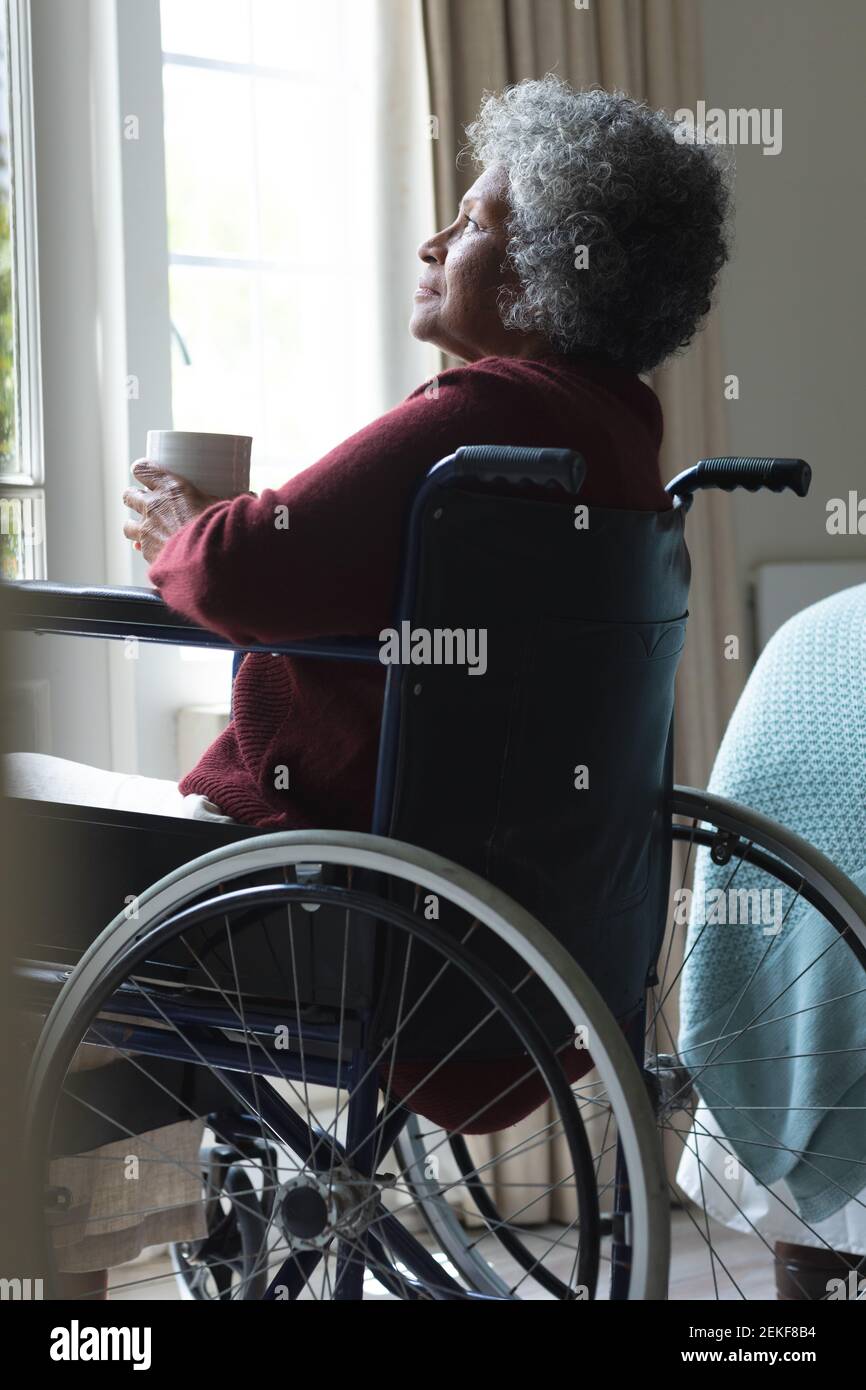 Une femme afro-américaine réfléchie tenant une tasse de café regarde de la fenêtre en étant assis sur w Banque D'Images