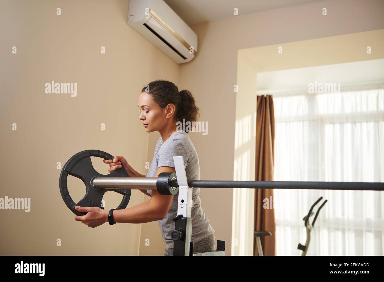 Une jeune femme pose un disque de métal sur une barbell olympique pendant l'entraînement de culturisme. Faire de l'exercice à la maison. Banque D'Images