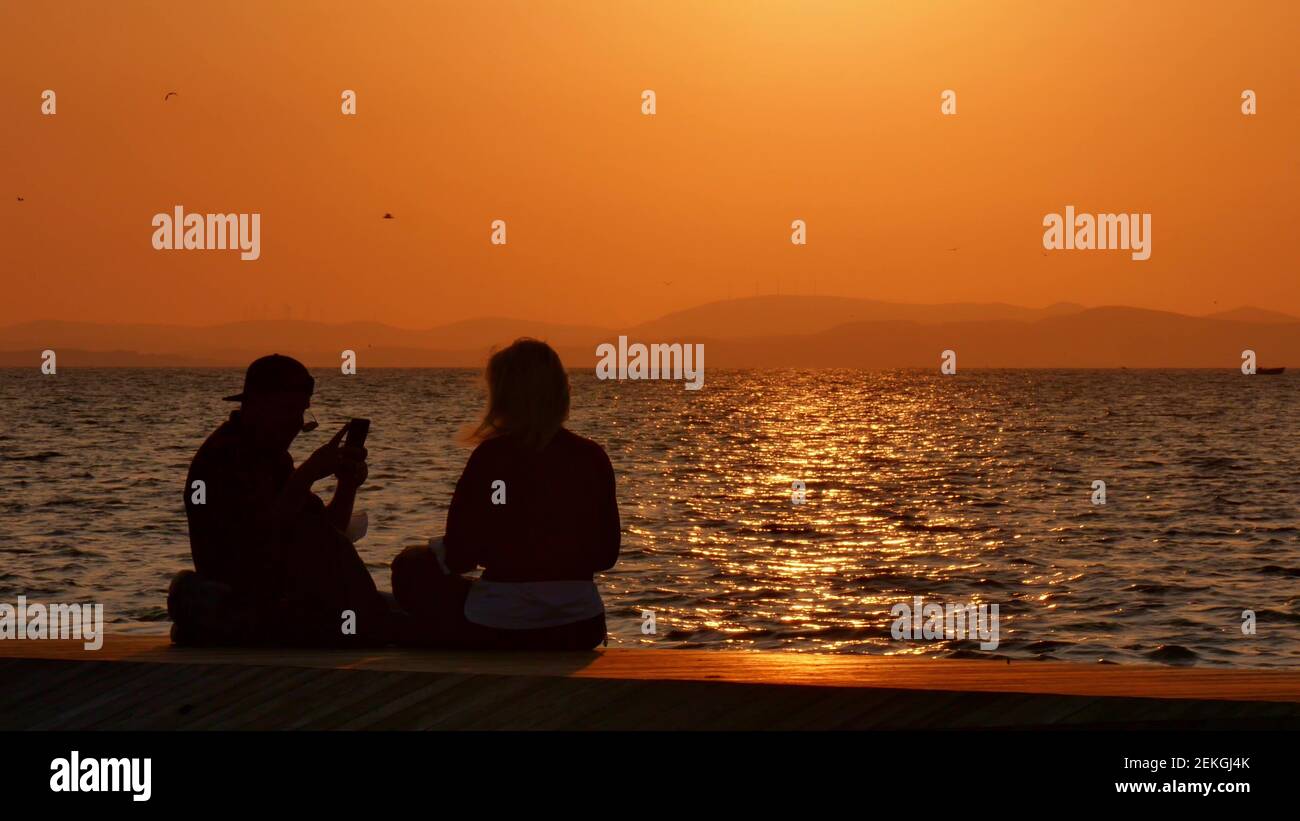 Silhouette d'un jeune couple prenant un selfie au coucher du soleil, avec une mer et le coucher du soleil en arrière-plan Banque D'Images