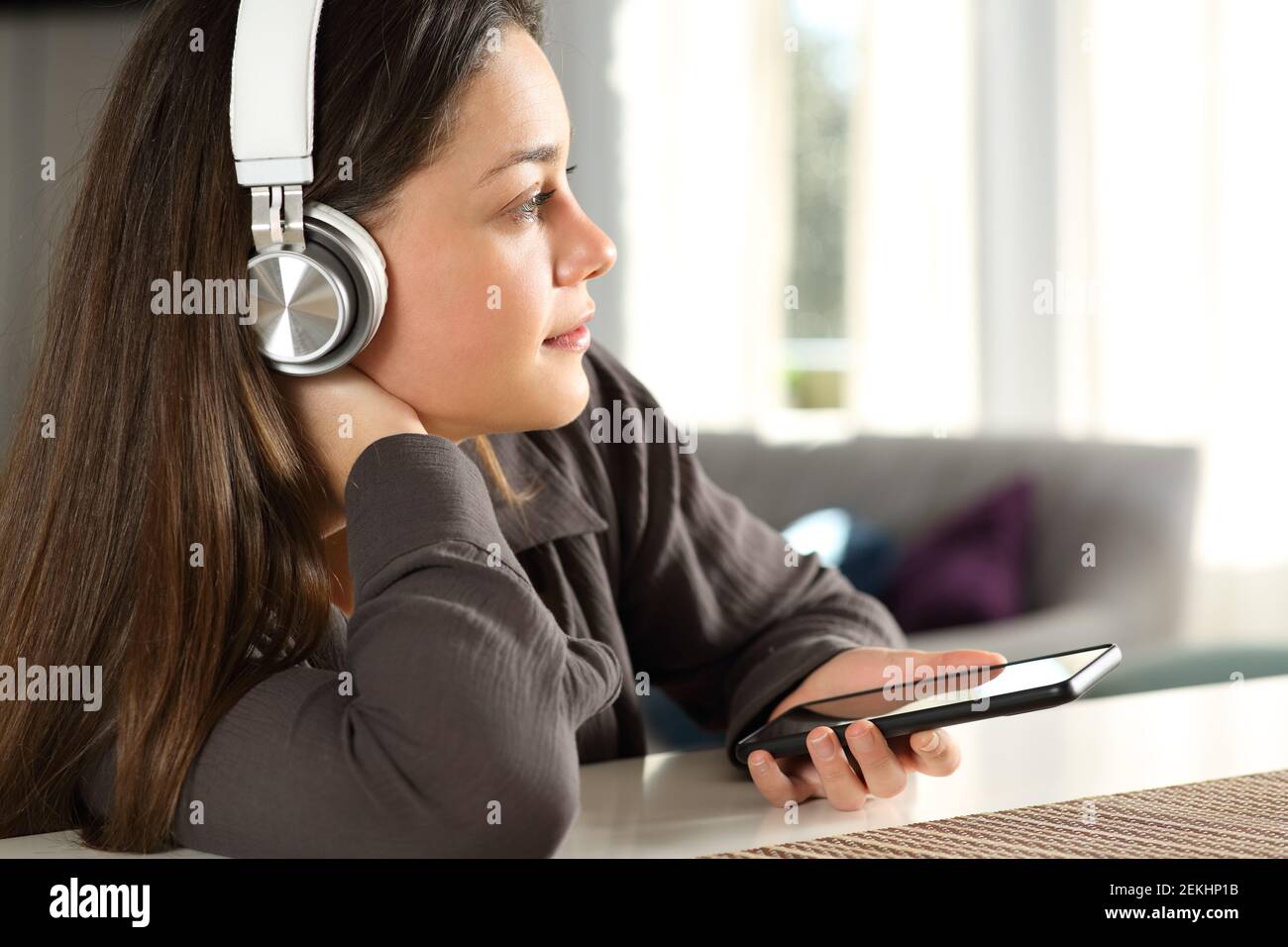 Femme pensive portant un casque sans fil qui envisage d'écouter de la musique à accueil Banque D'Images