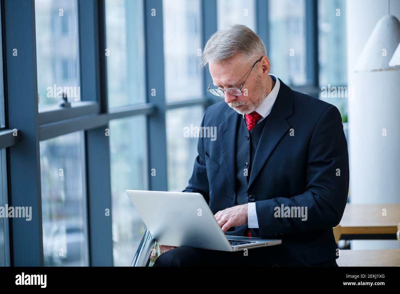 Sourire heureux directeur général pense à son développement de carrière réussi tout en se tenant debout avec un ordinateur portable dans son bureau près de l'arrière-plan d'une victoire Banque D'Images