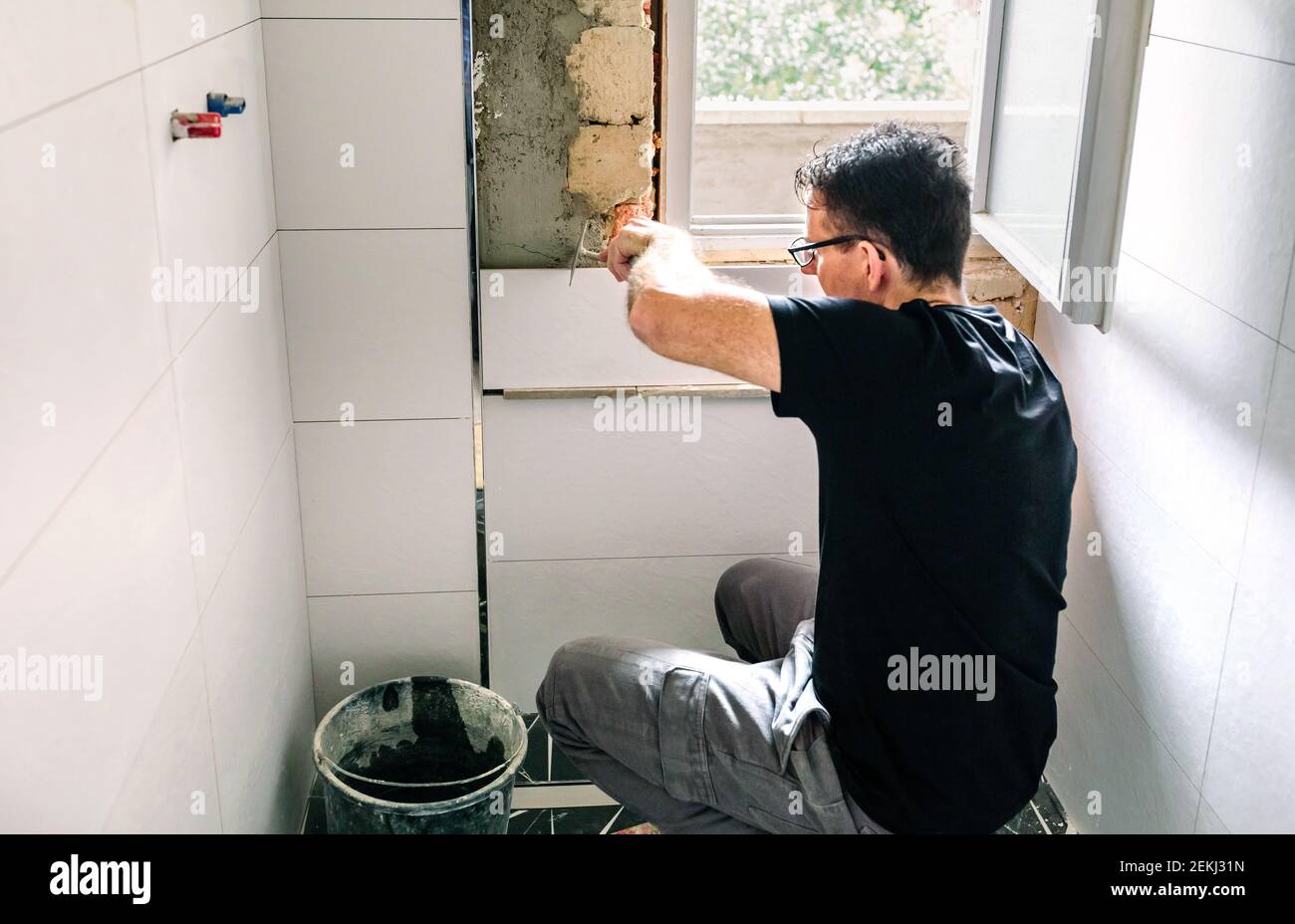 Couche de bricklayer posant le carrelage sur le mur avec une spatule Banque D'Images