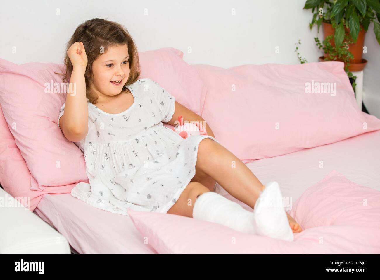 Une adolescente à l'esprit positif se trouve sur un lit dans une coulée sur sa jambe, avec une cheville cassée. La jambe de l'enfant est cassée, fracture osseuse Banque D'Images
