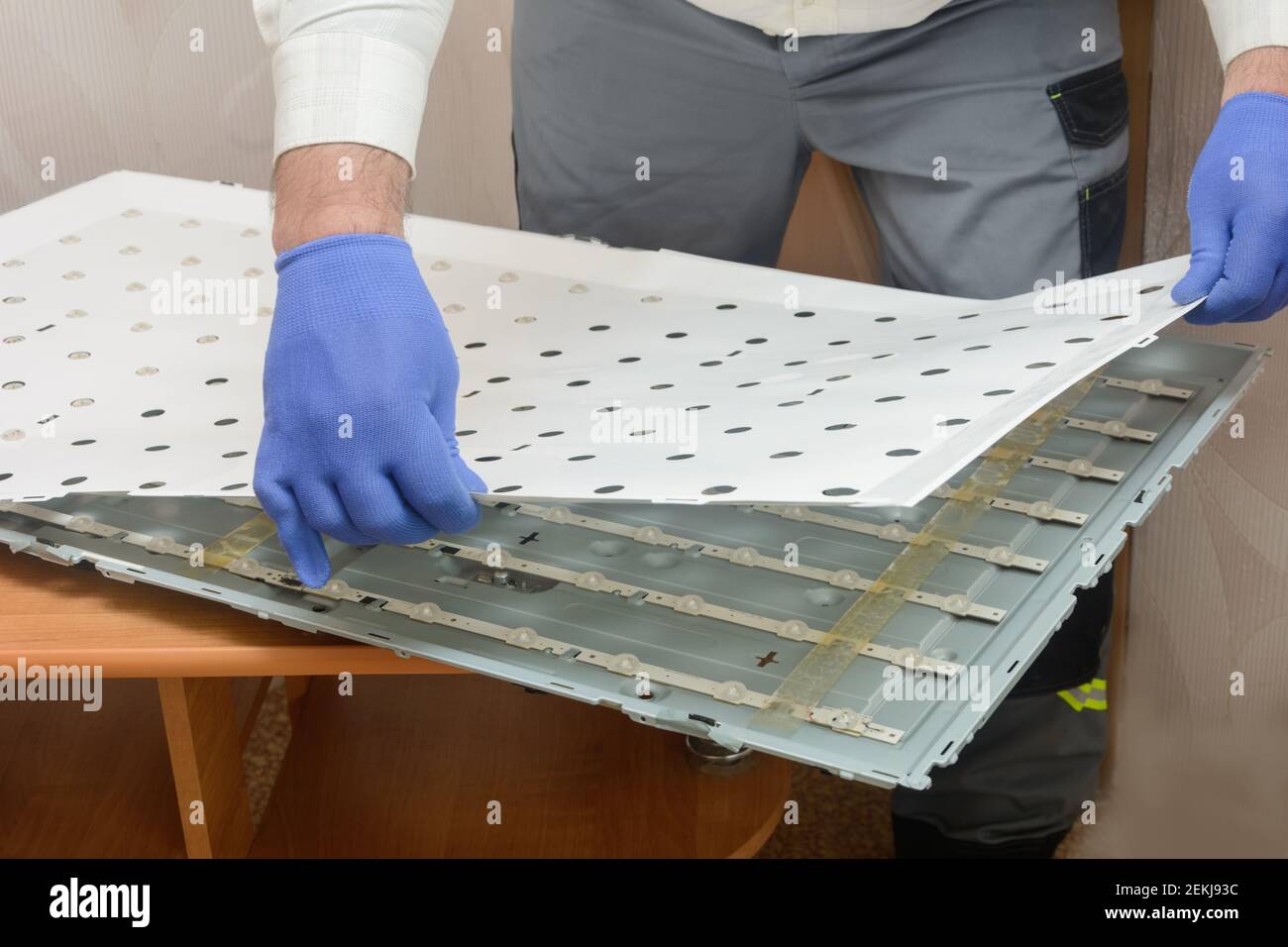 Réparation de la TV LCD. L'assistant supprime la feuille blanche de l'organiseur du boîtier du moniteur. Remplacement des bandes de la carte des voyants, dépannage. Banque D'Images