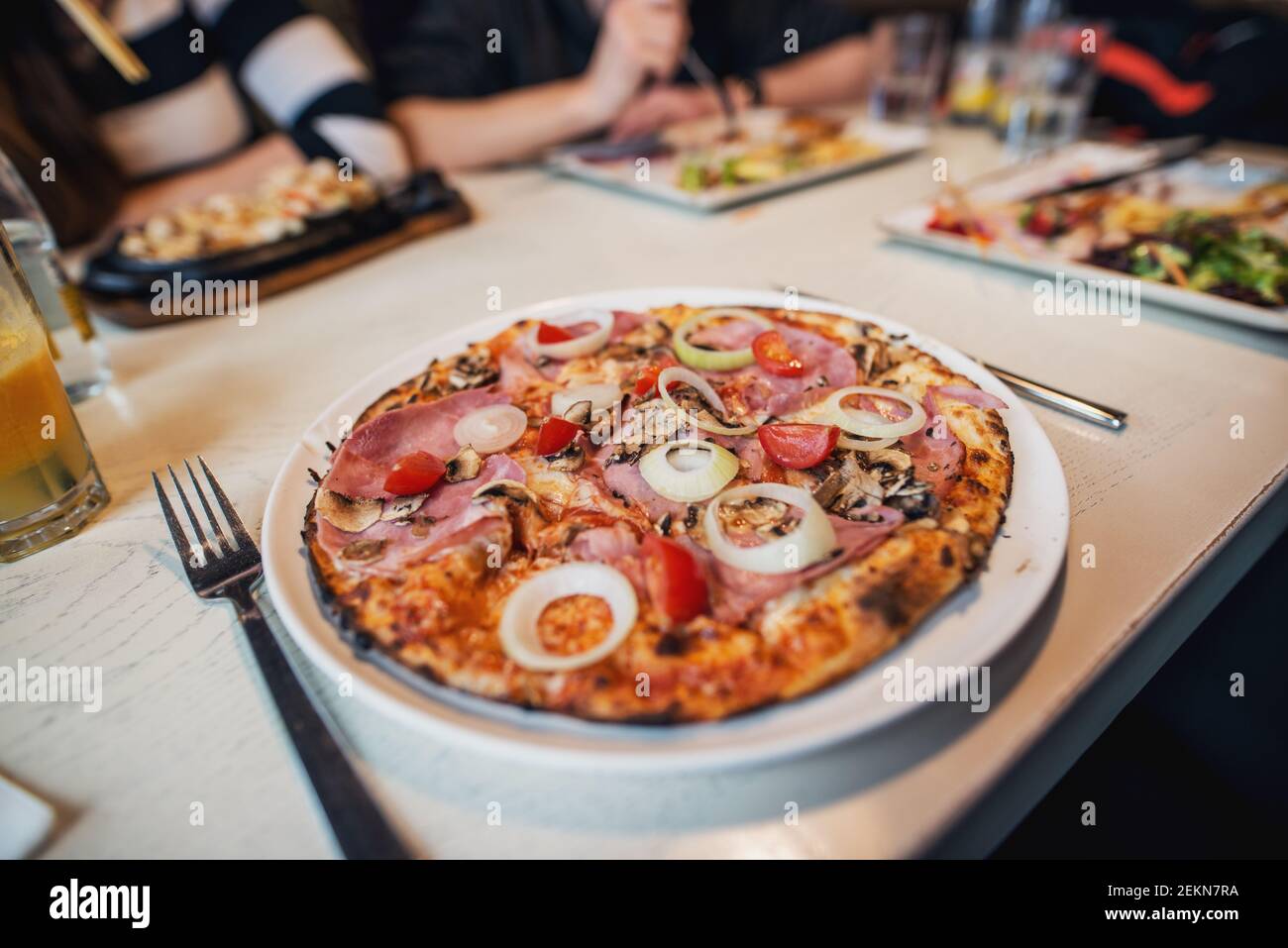 Une délicieuse pizza avec des tomates et des oignons sur la plaque blanche du restaurant pendant que les amis déjeunent. Banque D'Images