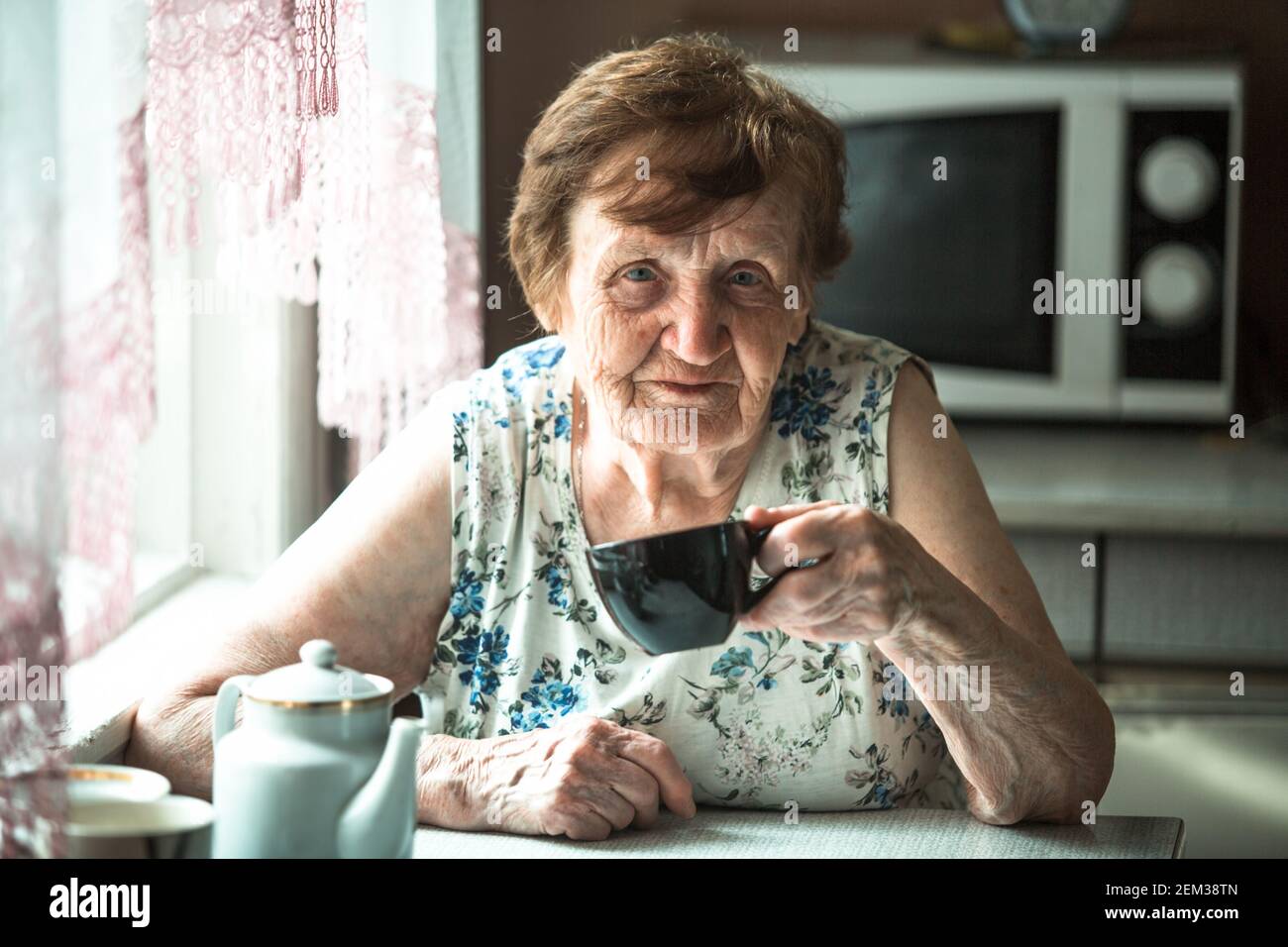Portrait d'une vieille femme qui boit du thé chez elle. Banque D'Images