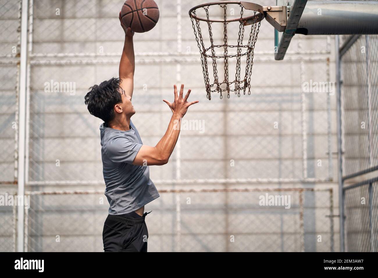 jeune homme asiatique adulte joueur de basket-ball essayant une dunk sur un terrain extérieur Banque D'Images