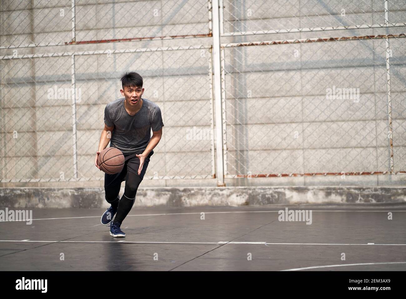un jeune homme asiatique essaie de jouer un dunk sur un terrain extérieur Banque D'Images