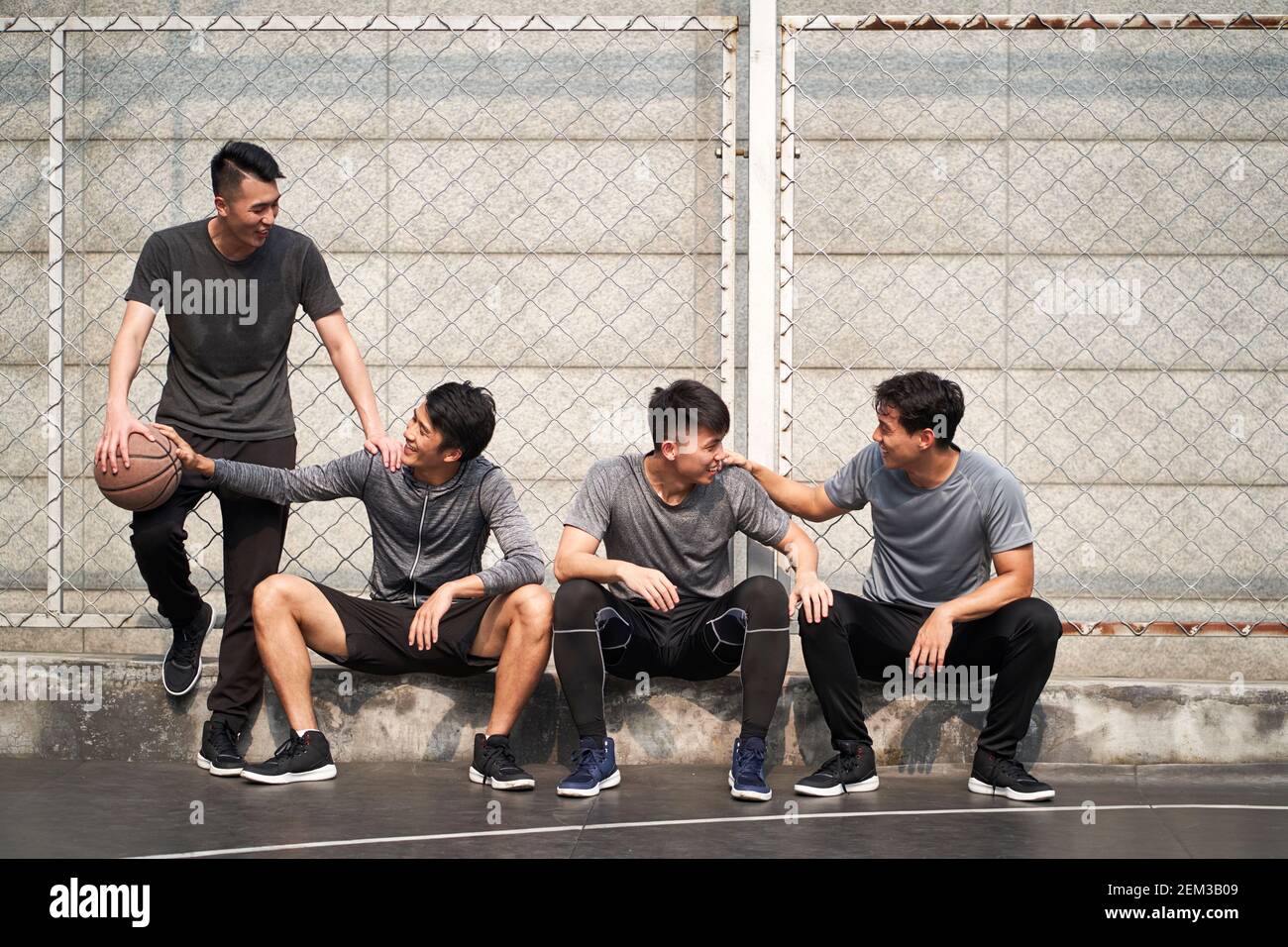 groupe de quatre jeunes hommes asiatiques se reposant sur un court de basket-ball extérieur pour discuter en toute tranquillité Banque D'Images