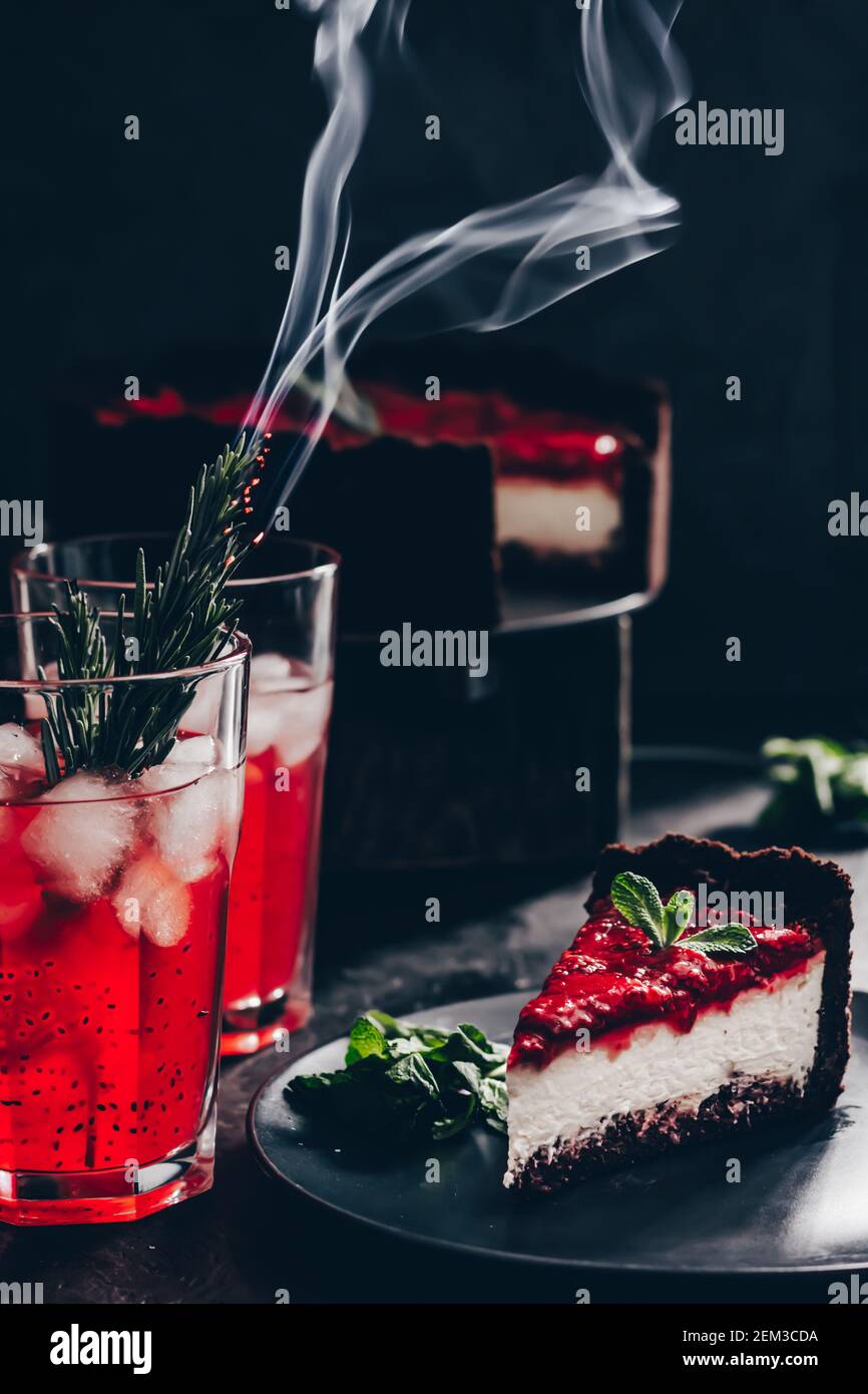 Composition incroyable avec cheesecake à la fraise et boisson à la fraise au romarin. Seulement une partie du cheesecake en foyer et une particule d'un verre de d Banque D'Images