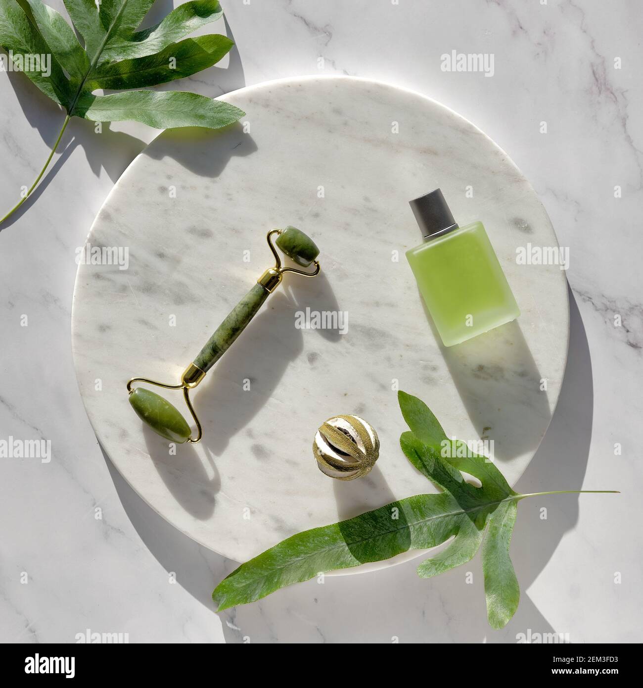 Rouleau facial Jade pour massage du visage, bouteille en verre à huile  essentielle. Vue de dessus sur un podium rond en marbre sur une table en  pierre assortie à une fougère exotique