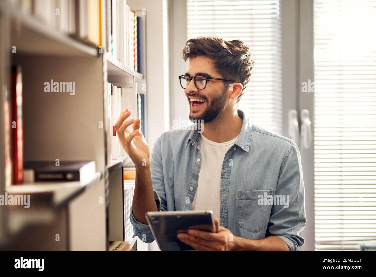 Gros plan des jeunes heureux beau lycéens holding une tablette et de célébrer après avoir trouvé un livre de la internet sur la bibliothèque dans le l Banque D'Images