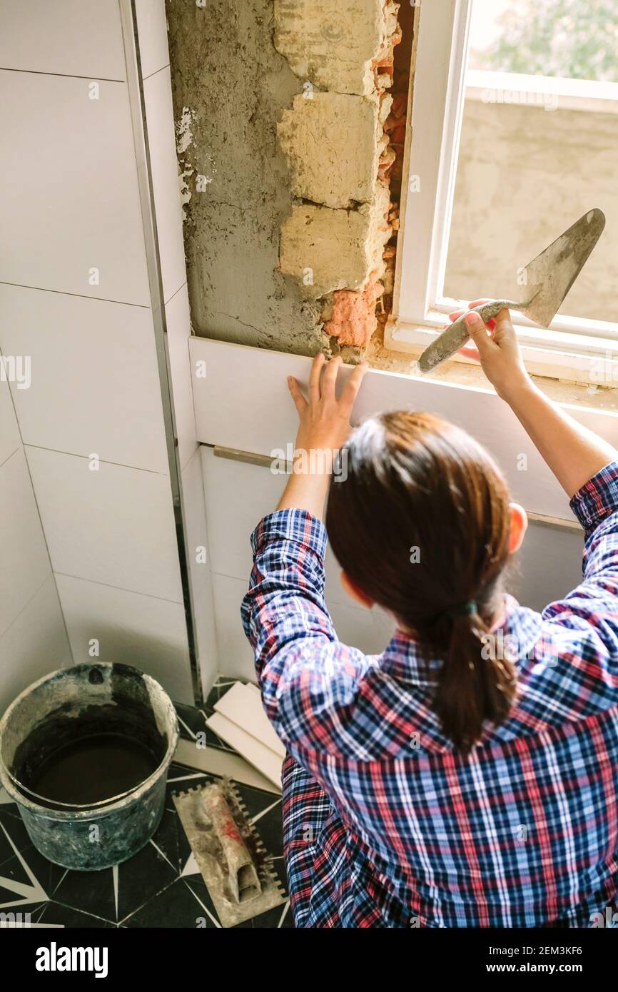 Couche de bricklayer posant le carrelage sur le mur avec une spatule Banque D'Images