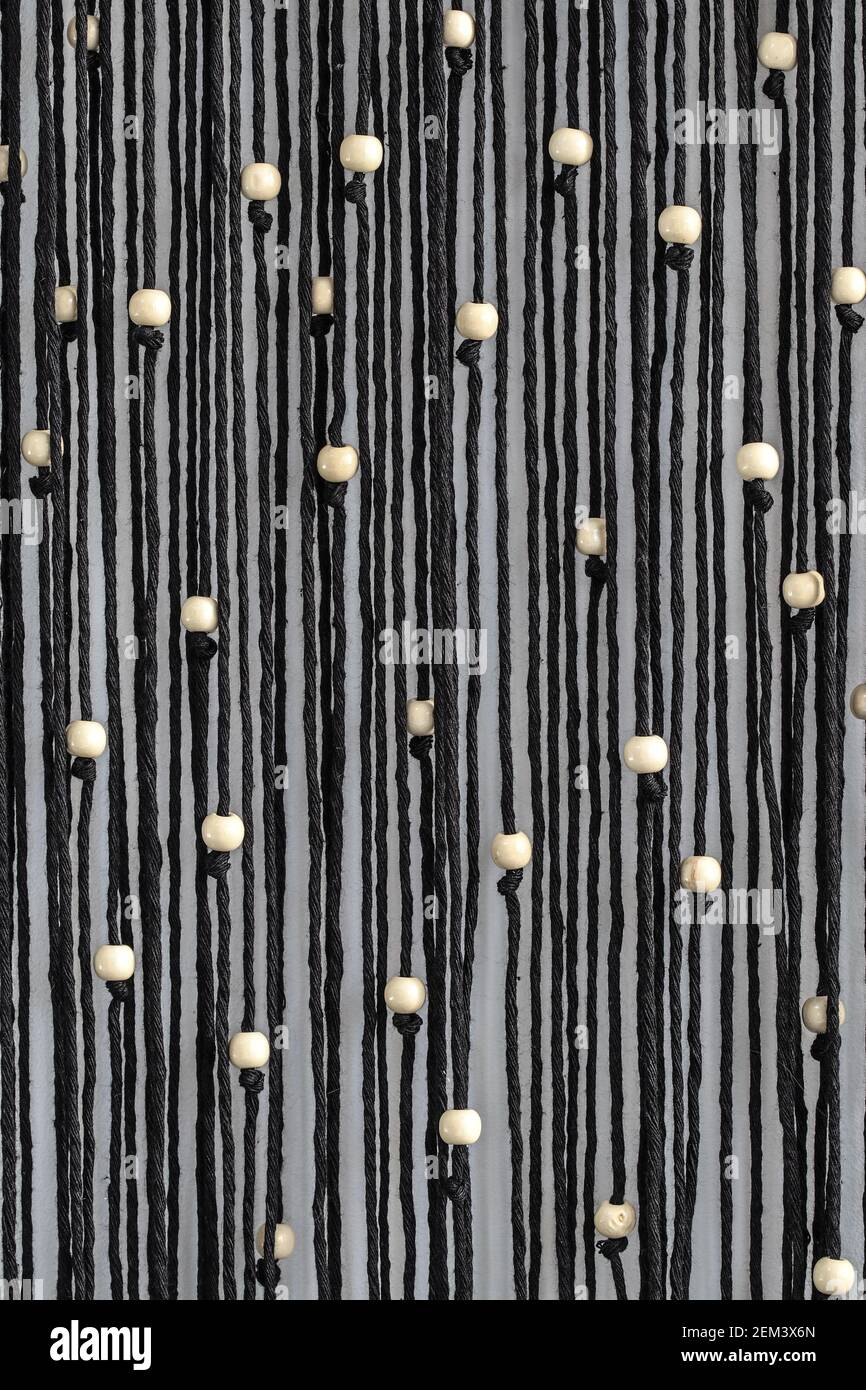 Cordes noires avec perles blanches macrame accrochée sur le mur abstrait arrière-plan Banque D'Images