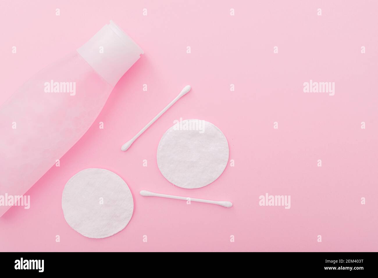 Composition simple avec lotion en flacon en plastique, tampons en coton et bâtonnets sur fond rose, vue du dessus, disposition Banque D'Images