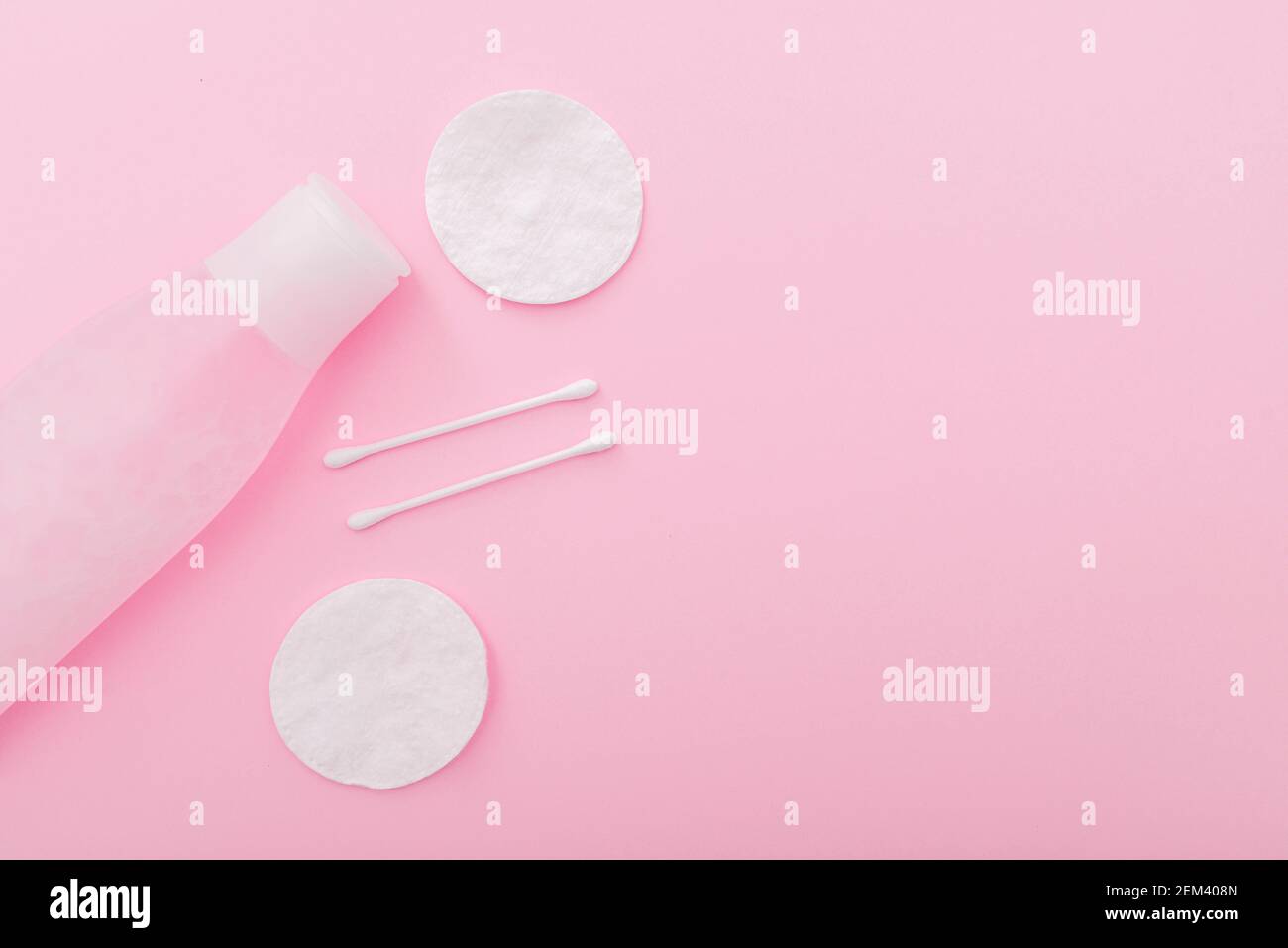 Composition simple avec lotion en flacon en plastique, tampons en coton et bâtonnets sur fond rose, vue du dessus, disposition Banque D'Images