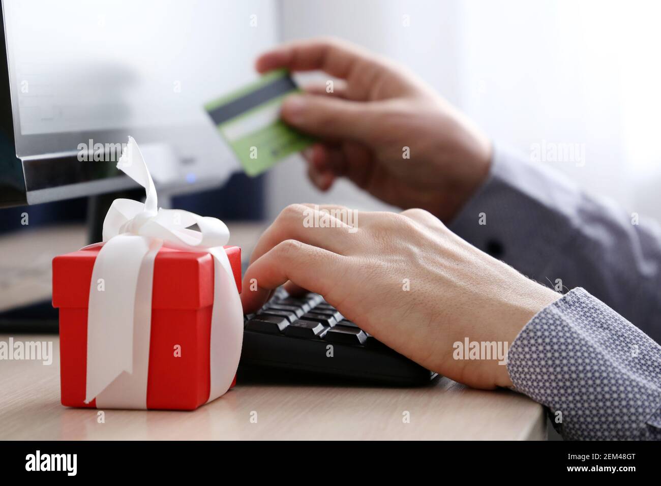 Homme avec carte de crédit assis sur le clavier de PC et boîte cadeau rouge. Concept d'achat d'un cadeau, d'achat en ligne et de paiement Banque D'Images