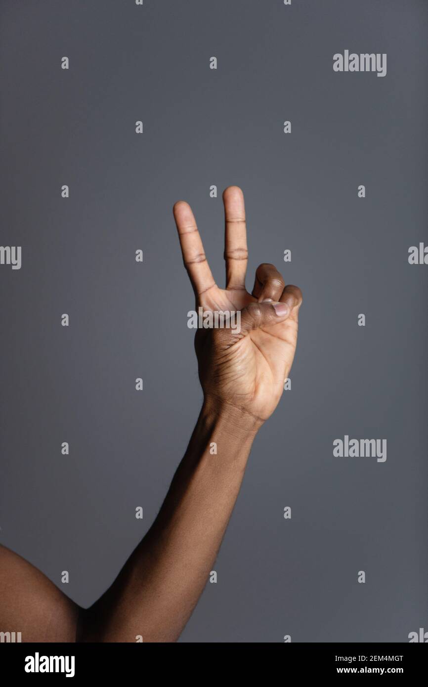 La main afro-américaine fait un geste de paix sur fond gris. Banque D'Images