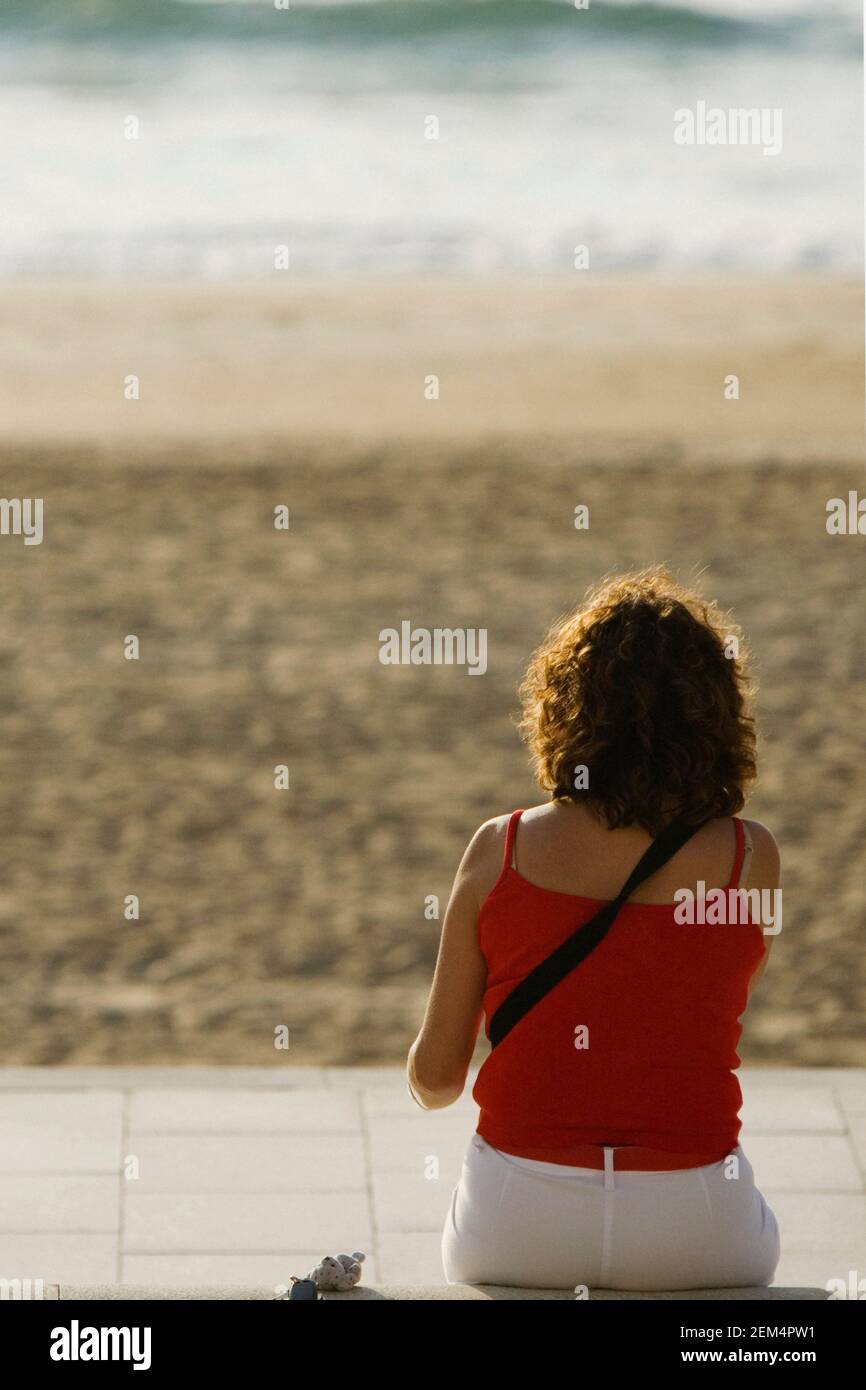 Vue arrière d'une femme assise sur la plage Banque D'Images