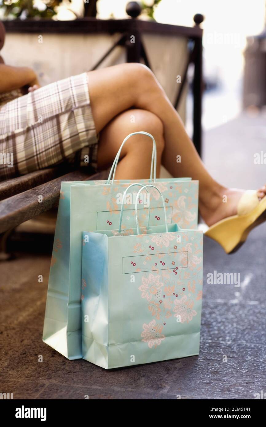 Vue en coupe basse d'une femme avec ses jambes croisées assis sur un banc près de deux sacs à provisions Banque D'Images