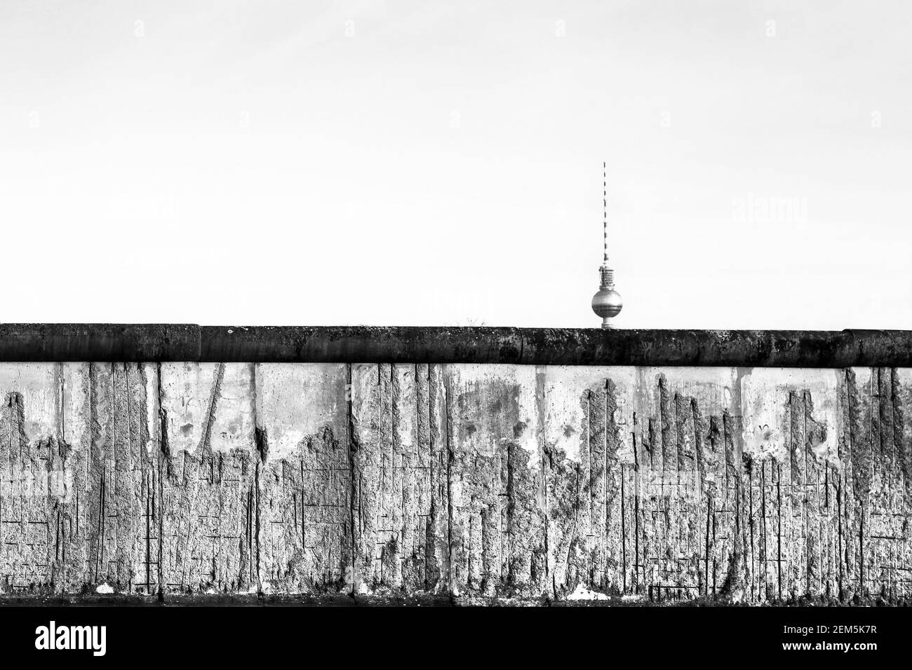 Mur de Berlin la section abîmée d'origine avec des barres de fer exposées couvrant en partie la tour de télévision (Berliner Fernsehturm) loin à l'horizon. Noir an Banque D'Images