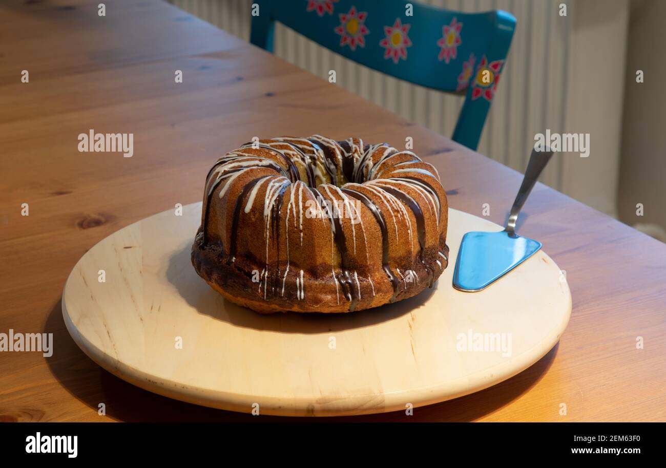 gâteau brun enrobé de sucre sur une platine blanche avec pelle à gâteau en argent, chaise bleue avec motif floral en arrière-plan Banque D'Images