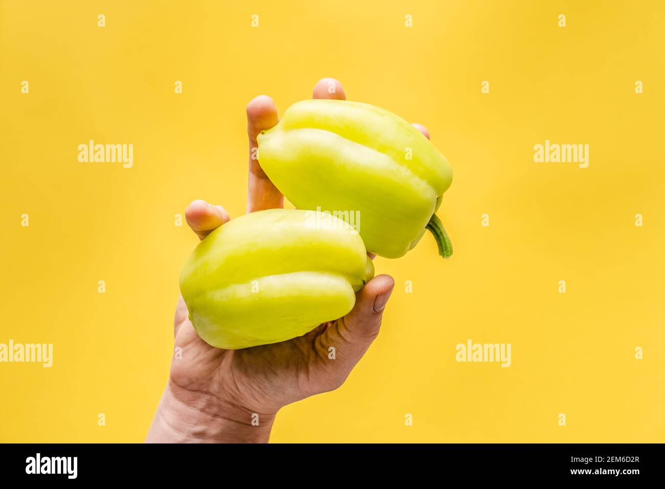 Main de la personne inconnue tenir des poivrons paprika frais bio sur fond jaune avec espace de copie - moderne sain manger végétarien ou végétalien Banque D'Images