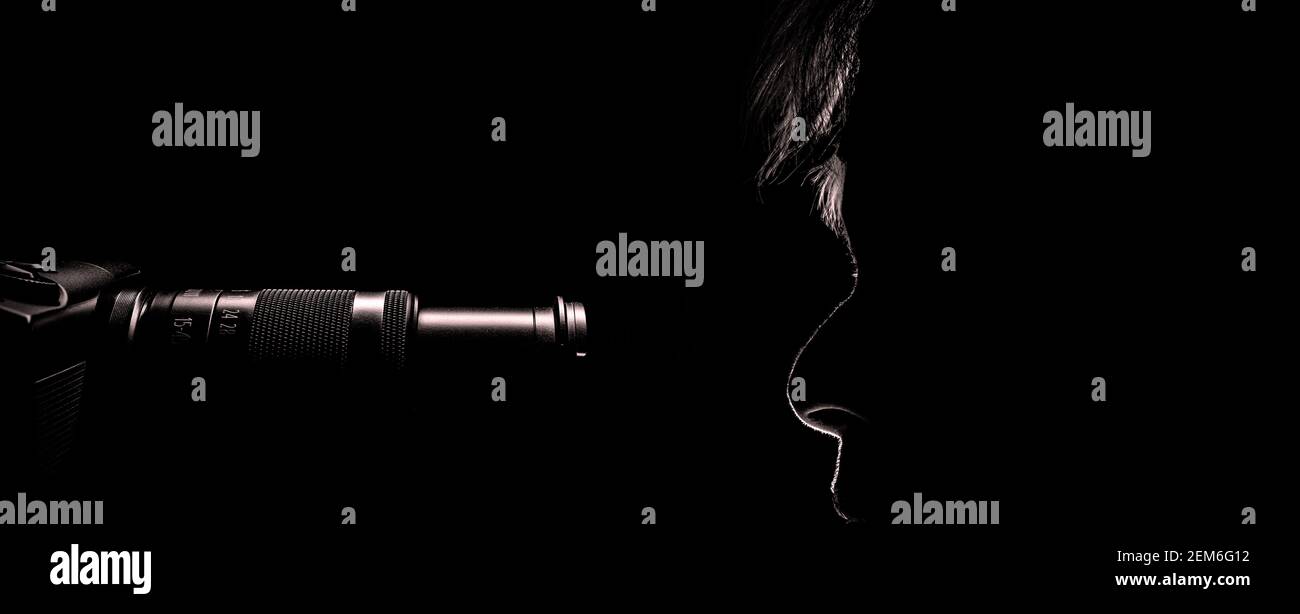 dans l'obscurité du studio, les lignes de contour du profil d'une femme émergent ainsi que la caméra l'observant. Face à face. Banque D'Images