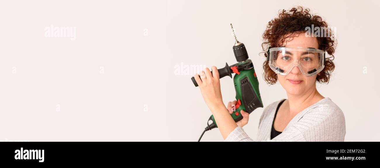 Une femme caucasienne aux cheveux bouclés tient un exercice dans ses mains, prête à faire des améliorations à la maison. Elle porte une chemise grise. Arrière-plan blanc. Lumière naturelle. Banque D'Images