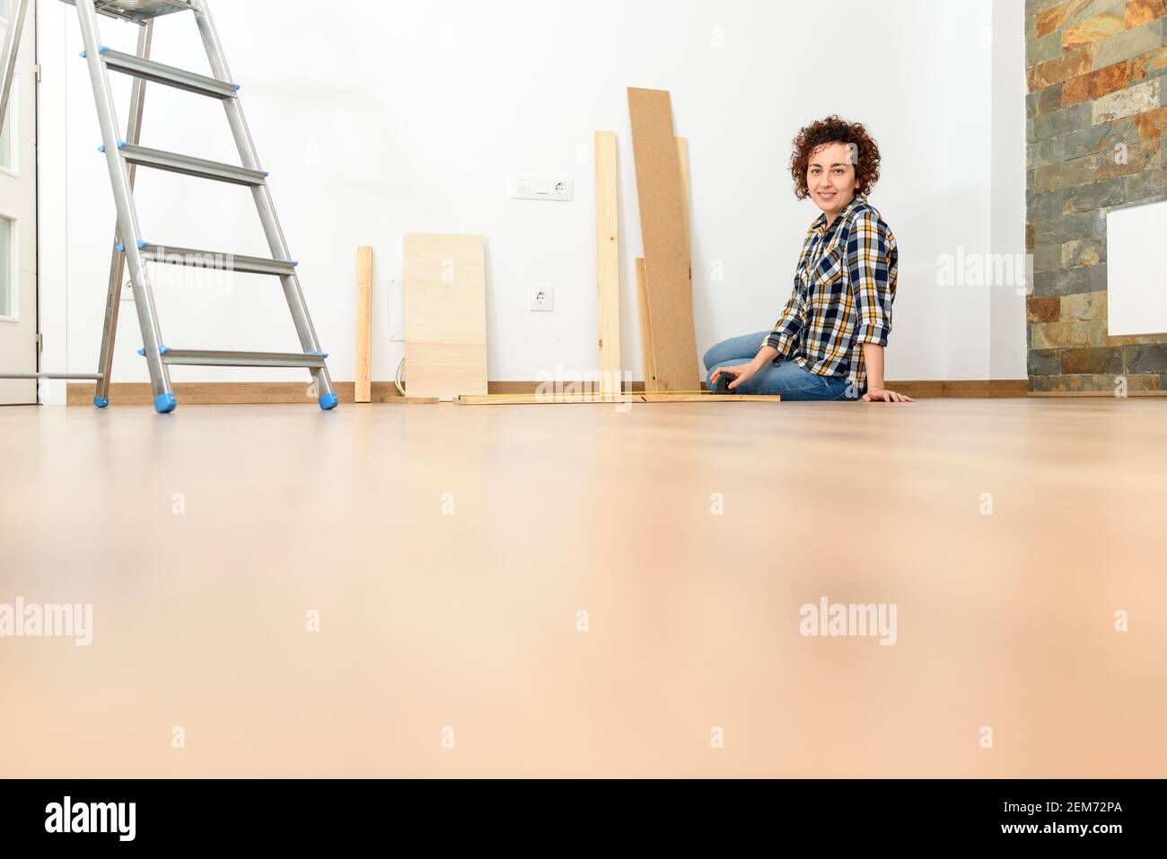 Jeune personne faisant du bricolage à la maison. Photographie au niveau du sol. Lumière naturelle. Mur blanc. Banque D'Images