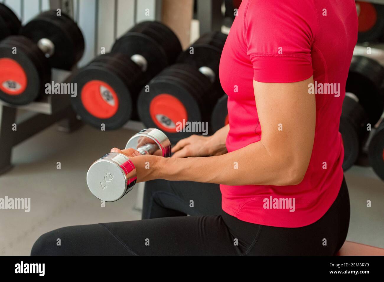 Vue arrière d'une jeune femme tenant des haltères et des biceps de train dans la salle de sport moderne. Mise au point sélective Banque D'Images
