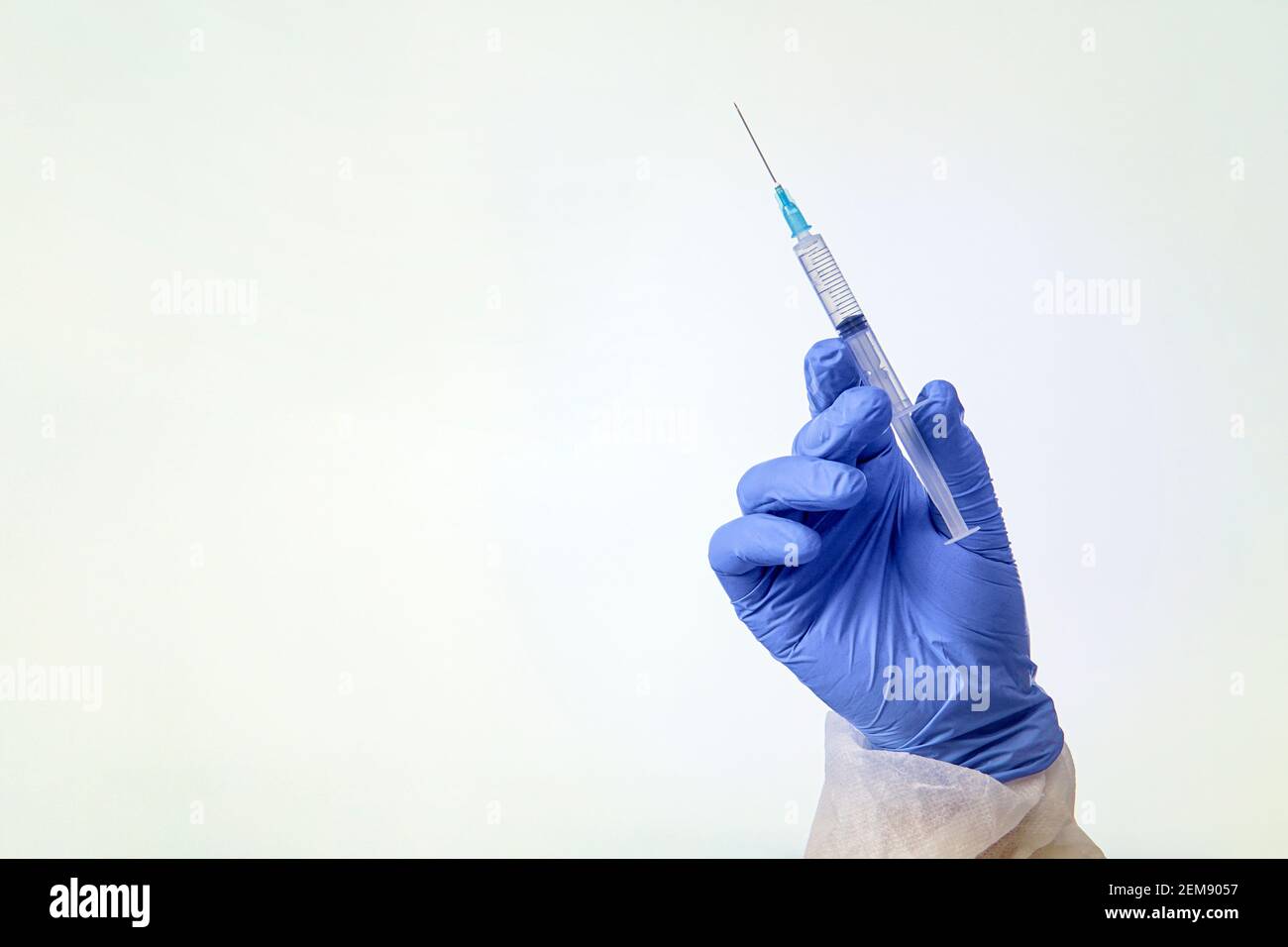 Main portant un gant de protection bleu tenant une seringue isolée blanc Banque D'Images