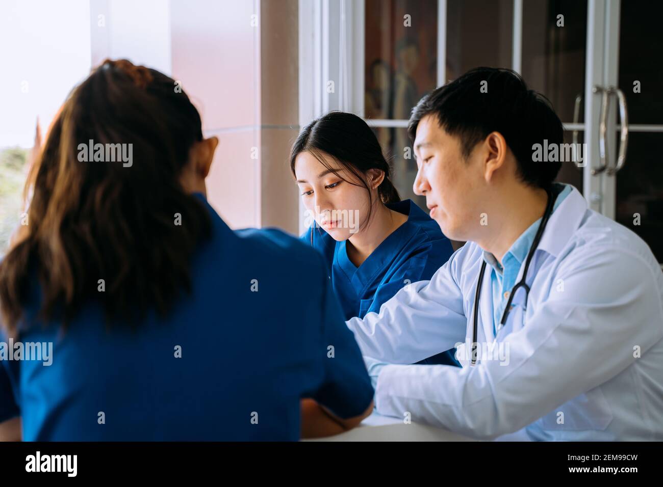 Groupe de jeunes asiatiques, hommes et femmes, médecin et infirmière s'asseoir pendant la pause dans la cantine et discuter de cas sérieux de patient à l'hôpital Banque D'Images