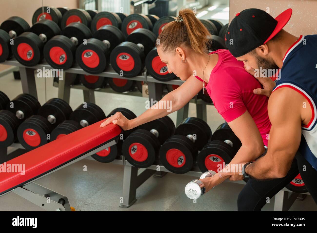 Entraîneur personnel entraîneurs jeune jolie femme faisant dumbbell biceps entraînement dans la salle de gym. Mise au point sélective Banque D'Images