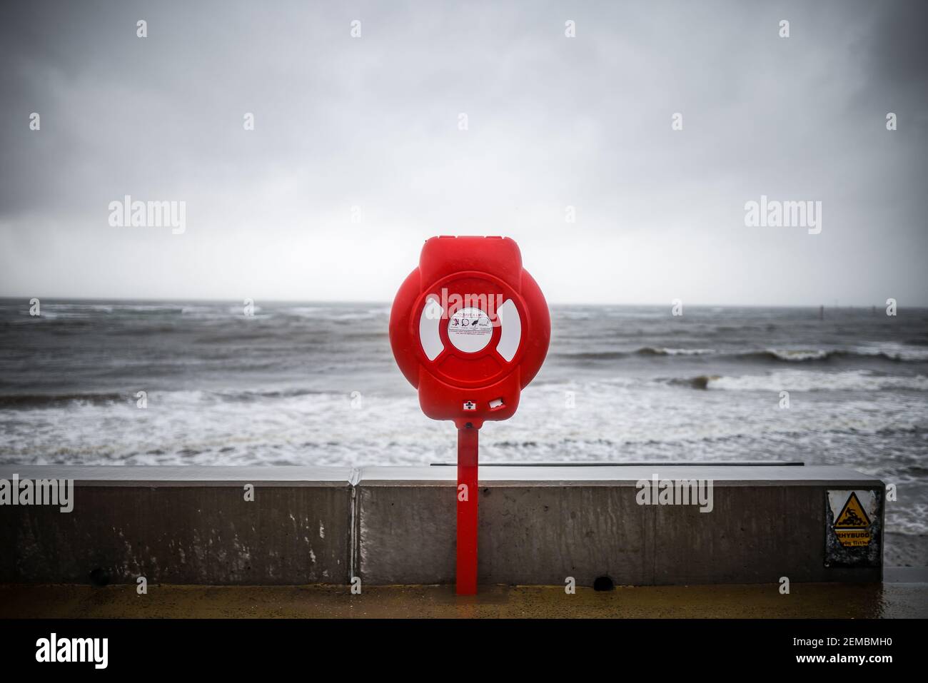 Rouge vif moderne bouée de sauvetage avertissement sur la côte de l'océan ciel de tempête. Équipement de sauvetage preserver poste d'urgence pour aider à prévenir la noyade en mer Banque D'Images