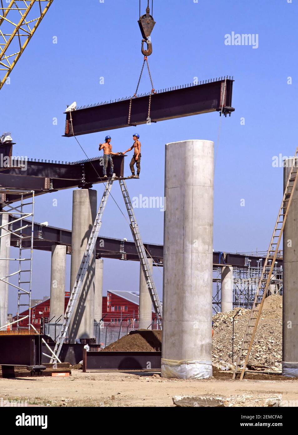 Historique 1984 archive view des travaux en cours sur le chantier de construction du bâtiment du projet de transport d'infrastructure de génie civil bâtiment des années 1980, Canary Wharf section aérienne du chemin de fer London Docklands Light LDR une grue abaissant des poutres en acier sur des colonnes de béton avec deux hommes travaillant sur des échelles sans règles modernes de santé et de sécurité une image d'archive de la façon dont nous étions dans l'est de Londres Angleterre au Royaume-Uni dans les années 80 Banque D'Images