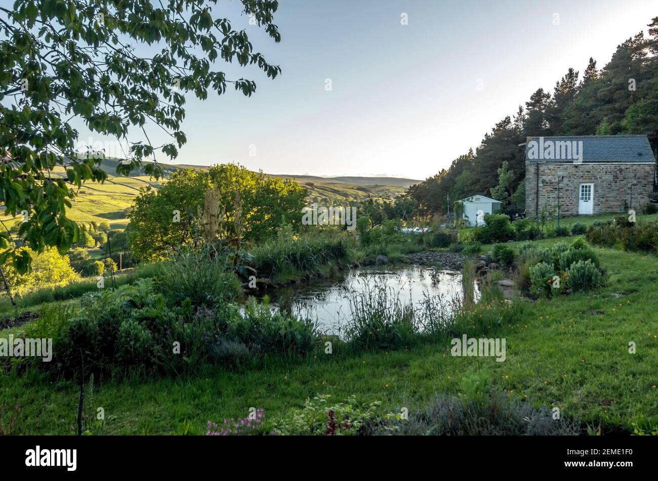 Un étang dans un jardin de campagne, avec une grange et les Pennines du Nord ensoleillées en arrière-plan Banque D'Images