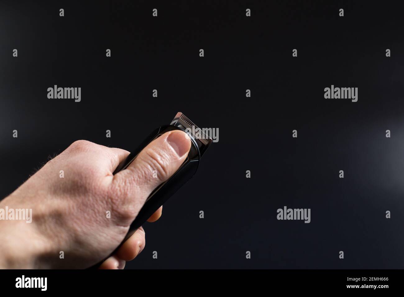Main de l'homme tenant la tondeuse électrique pour le rasage, sur fond noir avec espace de copie. Banque D'Images