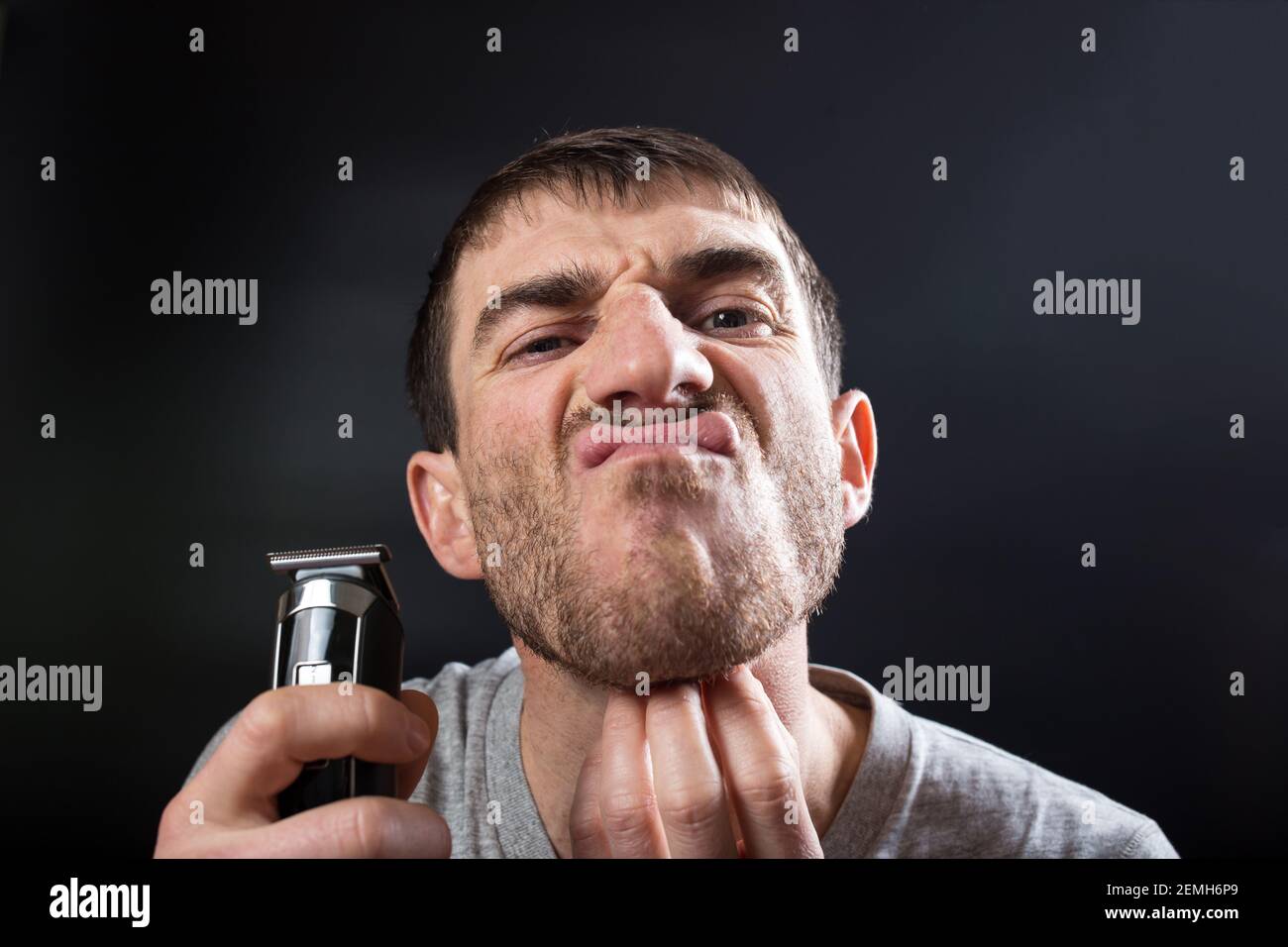 Homme avec une tondeuse pour se raser à la main, qui vous gratte la barbe et qui regarde la caméra. Banque D'Images