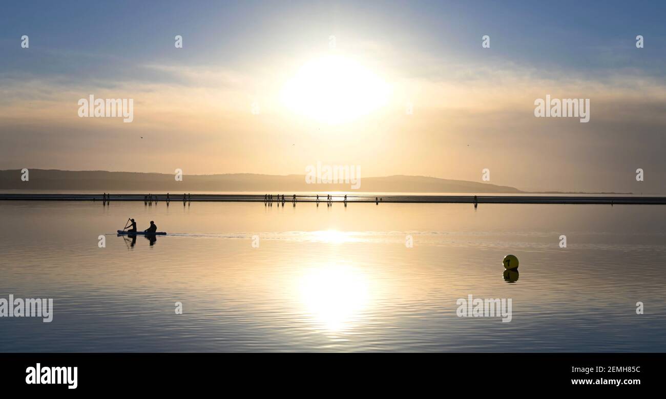 Deux personnes s'agenouillent sur une planche à aubes en pagayant le long du lac marin West Kirby pendant le coucher du soleil en février 2021. Banque D'Images