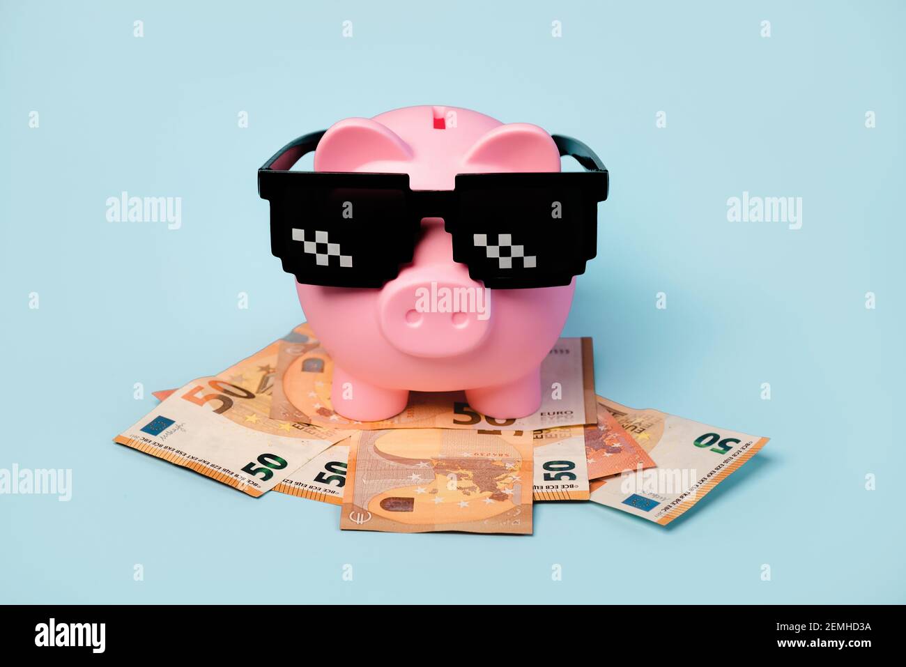 Banque d'argent rose avec lunettes de soleil noires et billets en euros sur fond bleu Banque D'Images