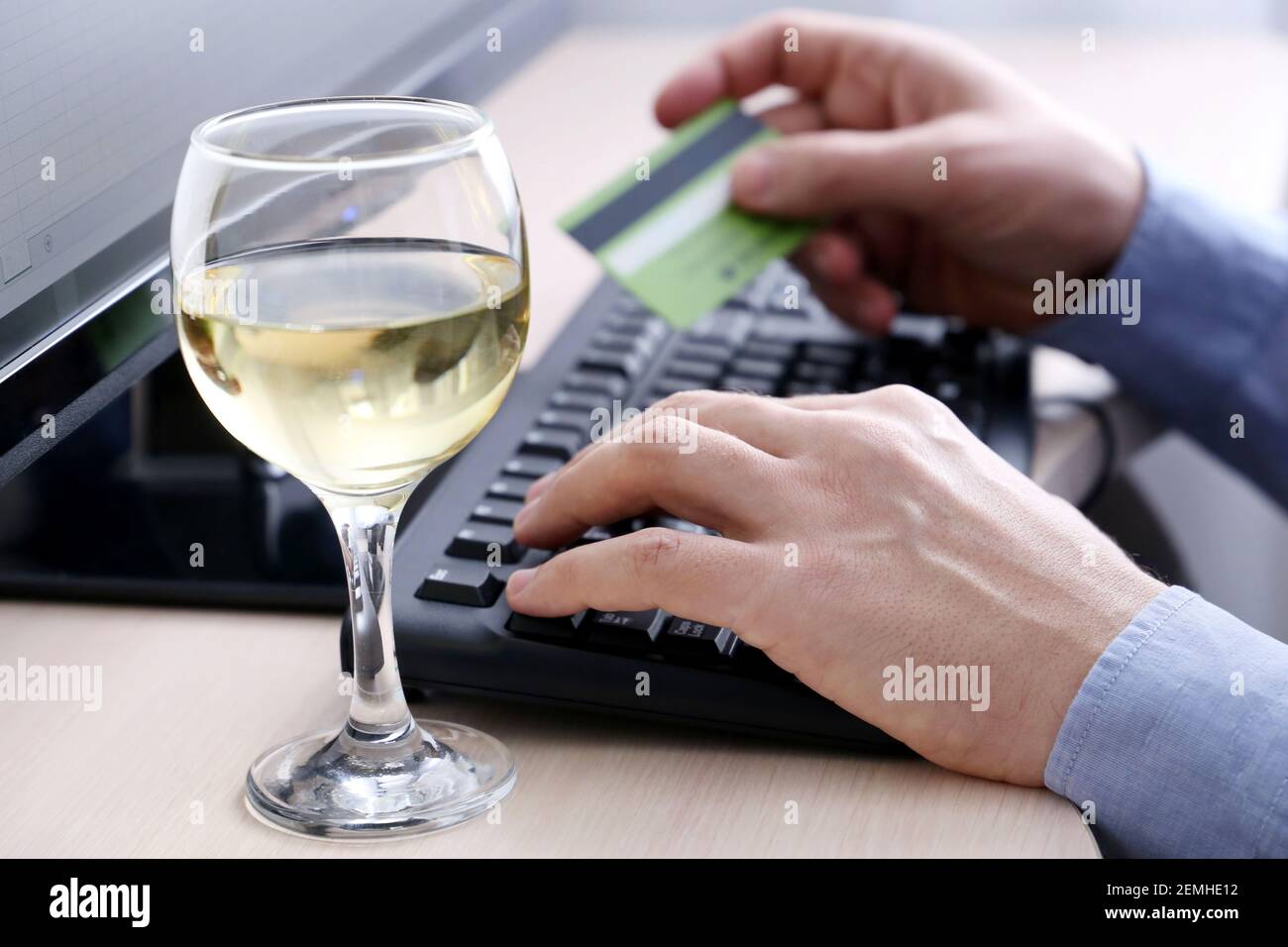 Homme tenant les types de carte de crédit sur le clavier de PC, vue défoqué à travers le verre de vin blanc. Concept de shopping en ligne sous l'alcool Banque D'Images