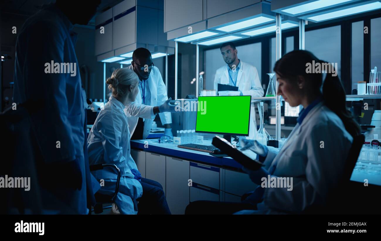 Réunion des laboratoires de recherche médicale : une équipe diversifiée de scientifiques utilisent un ordinateur personnel affichant un écran de clé Chroma vert. Laboratoire avancé de médecine Banque D'Images