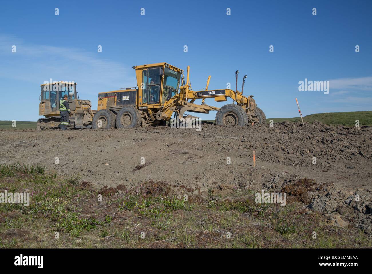 Bulldozer et niveleuse gradant la route pendant la construction estivale de la route Inuvik-Tuktoyaktuk, dans l'Arctique canadien. Banque D'Images