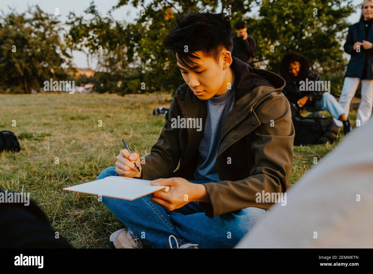 Jeune homme écrivant dans le livre au parc Banque D'Images