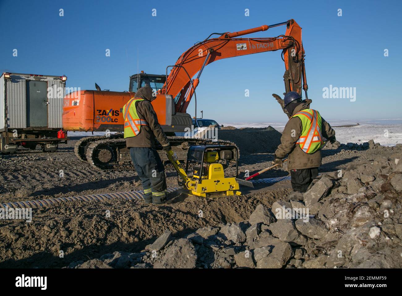 Des travailleurs et des excavateurs de sexe masculin installent un ponceau pendant la construction hivernale de la route Inuvik-Tuktoyaktuk, dans l'Arctique canadien. Banque D'Images