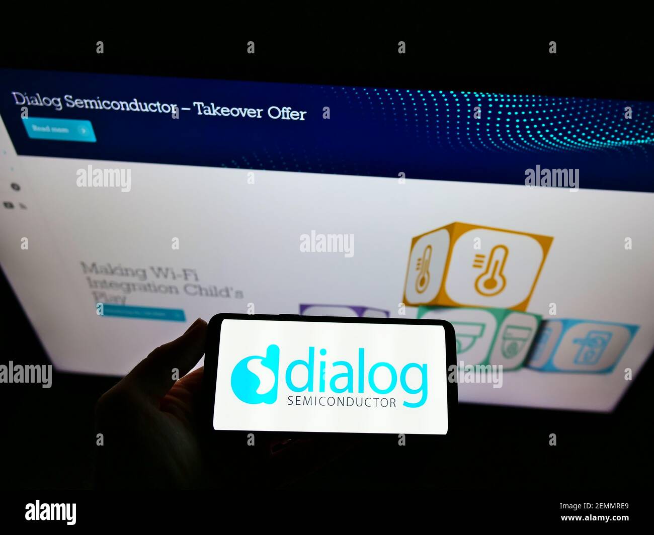 Personne tenant un smartphone avec le logo de la société d'ingénierie Dialog Semiconductor PLC à l'écran devant le site Web. Mise au point sur l'affichage du téléphone. Banque D'Images